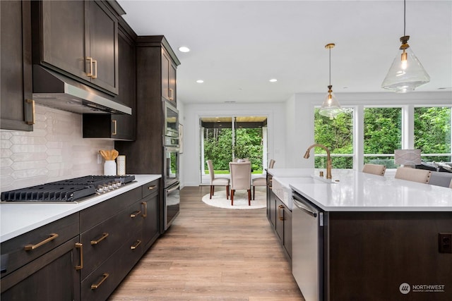 kitchen with appliances with stainless steel finishes, tasteful backsplash, sink, pendant lighting, and an island with sink