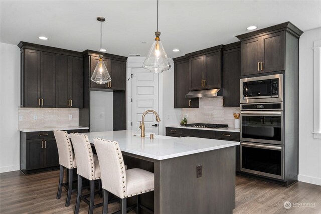 kitchen featuring appliances with stainless steel finishes, sink, dark hardwood / wood-style floors, hanging light fixtures, and an island with sink