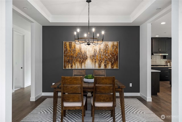 dining area featuring a notable chandelier, a raised ceiling, and dark wood-type flooring