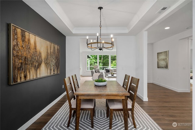 dining space featuring a tray ceiling, dark wood-type flooring, and a notable chandelier