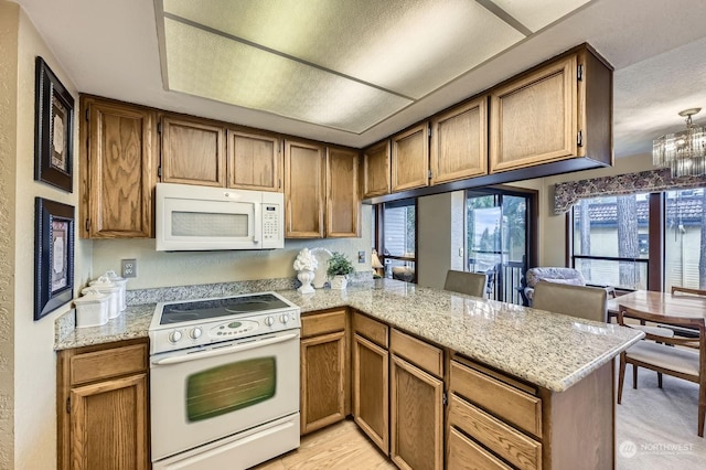 kitchen with light wood-type flooring, an inviting chandelier, white appliances, and kitchen peninsula