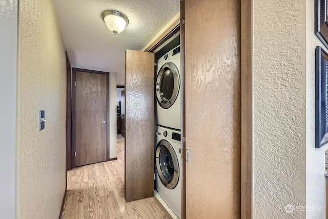 laundry area featuring stacked washer and dryer, a textured ceiling, and light wood-type flooring