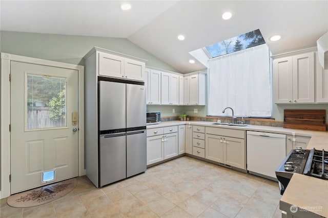 kitchen with stainless steel fridge, white cabinets, vaulted ceiling with skylight, sink, and dishwasher