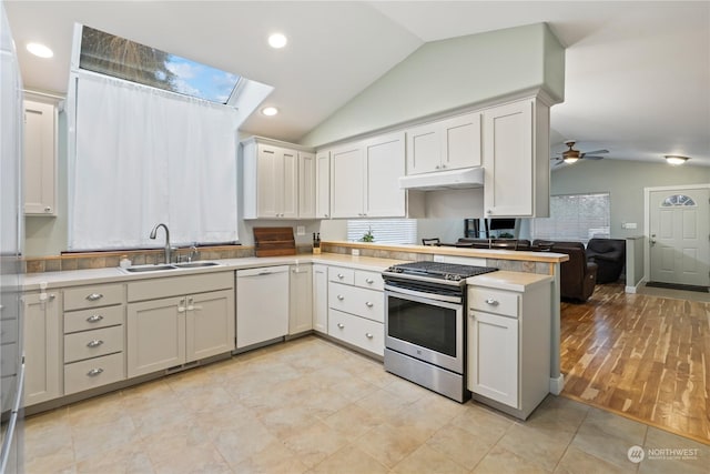 kitchen with dishwasher, stainless steel range, sink, vaulted ceiling with skylight, and white cabinets