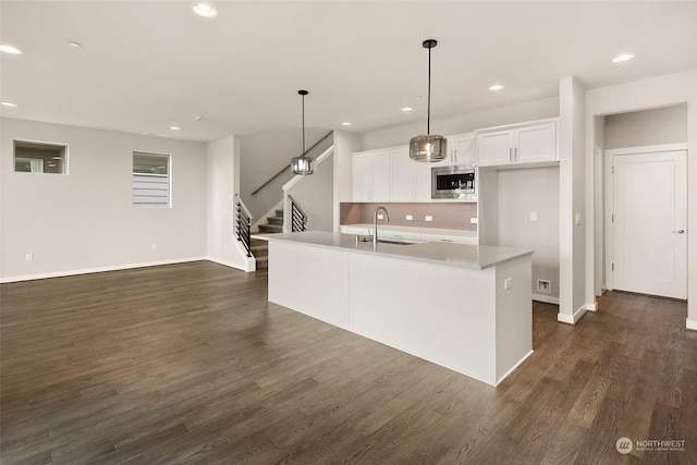 kitchen with white cabinetry, stainless steel microwave, sink, hanging light fixtures, and an island with sink