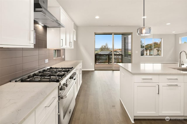 kitchen featuring light stone counters, high end stainless steel range oven, wall chimney range hood, decorative light fixtures, and white cabinets