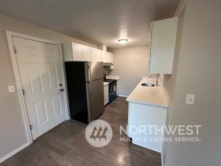 kitchen featuring black refrigerator, dark wood-type flooring, sink, range, and white cabinetry