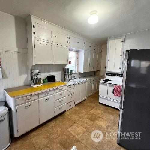 kitchen with stainless steel fridge, white cabinetry, and white electric stove