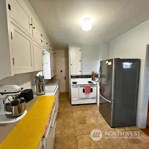 kitchen featuring white range with electric stovetop, white cabinetry, and stainless steel refrigerator