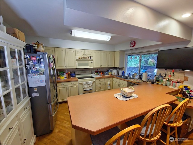 kitchen with kitchen peninsula, decorative backsplash, white appliances, and light wood-type flooring