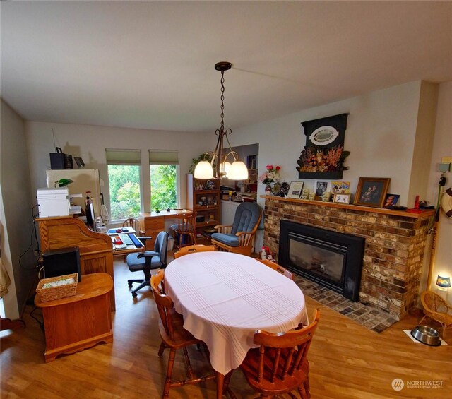 dining space featuring hardwood / wood-style floors, a brick fireplace, and a notable chandelier