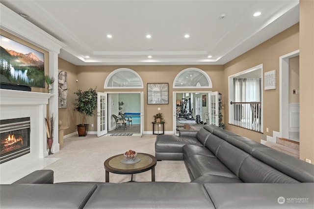 living room with a tray ceiling, a tile fireplace, french doors, and light colored carpet