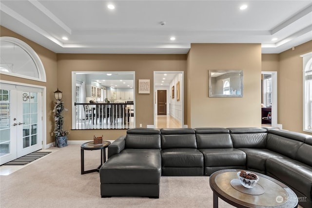 living room featuring a raised ceiling, light carpet, and french doors