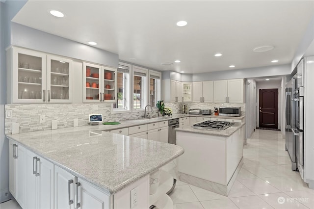 kitchen with light stone countertops, a center island, kitchen peninsula, white cabinets, and appliances with stainless steel finishes