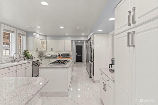 kitchen with light stone countertops, sink, a kitchen island, white cabinets, and appliances with stainless steel finishes