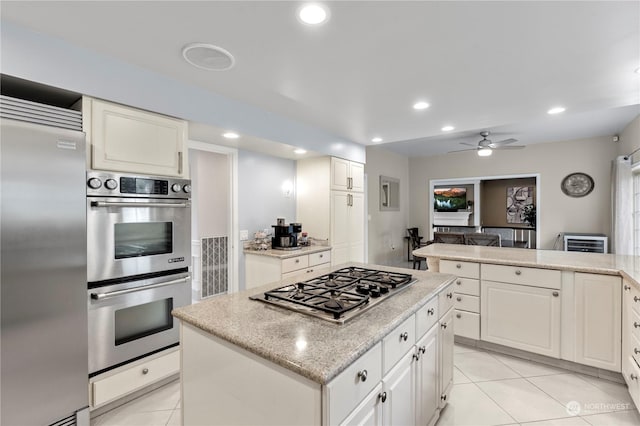 kitchen with appliances with stainless steel finishes, ceiling fan, light tile patterned floors, a center island, and white cabinetry