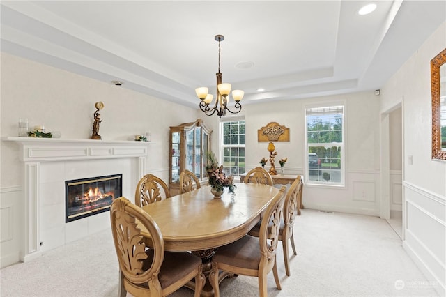 carpeted dining space with a chandelier, a raised ceiling, and a tiled fireplace