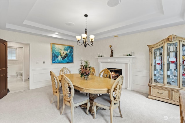 dining room featuring a notable chandelier, a raised ceiling, and light colored carpet