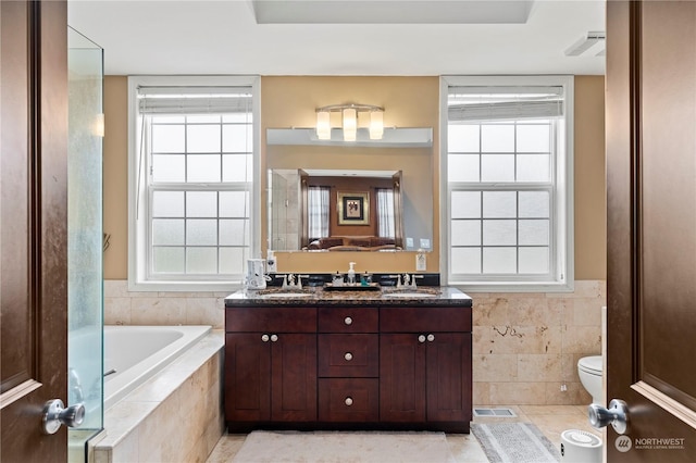 bathroom with vanity, a relaxing tiled tub, toilet, and a healthy amount of sunlight