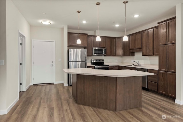 kitchen with sink, appliances with stainless steel finishes, decorative light fixtures, a kitchen island, and dark brown cabinetry