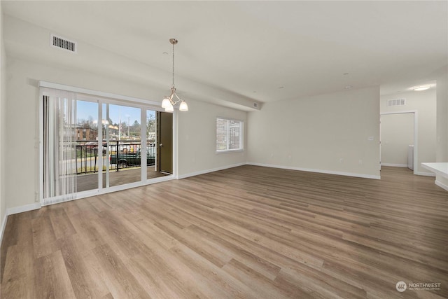 unfurnished living room featuring a notable chandelier and light hardwood / wood-style floors