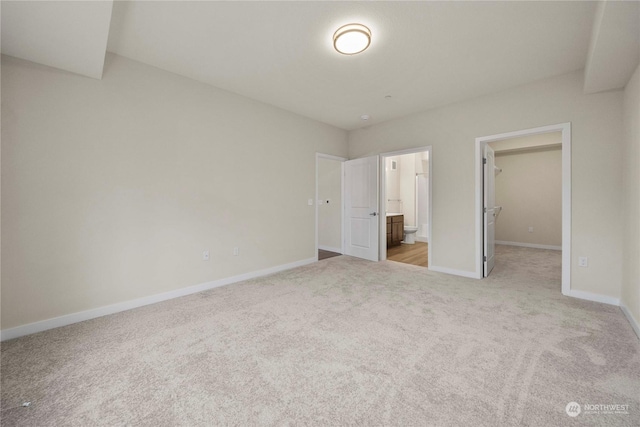 unfurnished bedroom featuring a walk in closet, ensuite bathroom, a closet, and light colored carpet