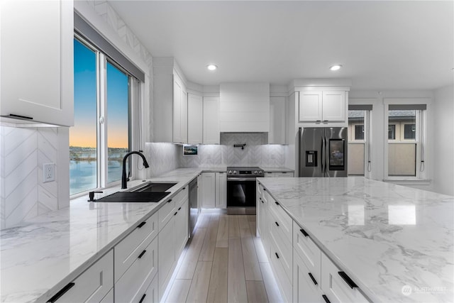 kitchen with a water view, sink, light stone counters, white cabinetry, and stainless steel appliances