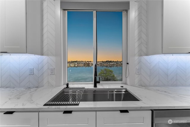 kitchen featuring white cabinets, sink, a water view, and light stone counters