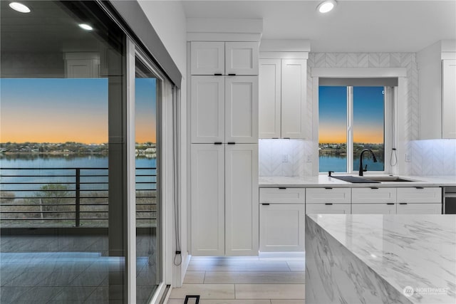 kitchen with white cabinets, a water view, sink, decorative backsplash, and light stone counters