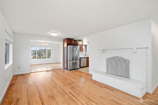 unfurnished living room with sink, a fireplace, a chandelier, and light wood-type flooring