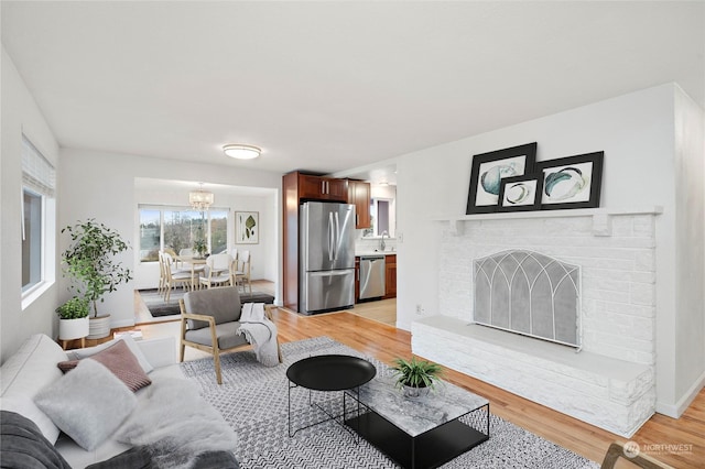 living room with an inviting chandelier, sink, light hardwood / wood-style floors, and a brick fireplace