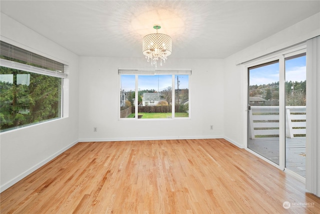 spare room with an inviting chandelier, plenty of natural light, and light hardwood / wood-style floors