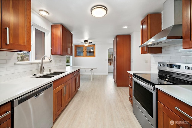 kitchen with sink, light hardwood / wood-style flooring, ceiling fan, stainless steel appliances, and wall chimney range hood