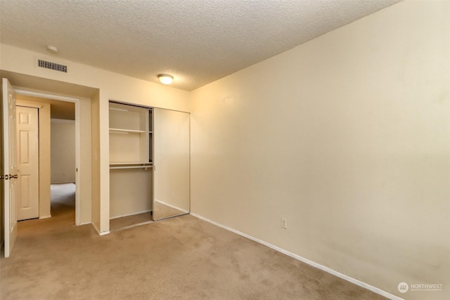 unfurnished bedroom featuring a textured ceiling, light colored carpet, and a closet