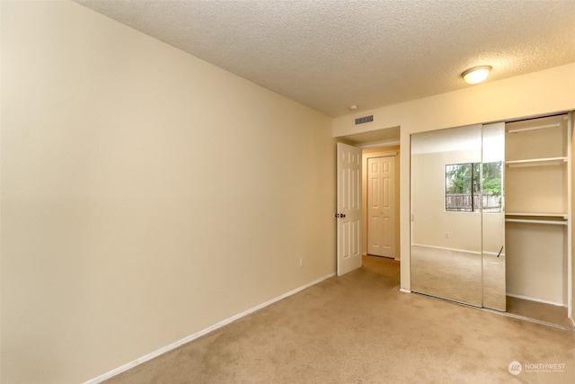 unfurnished bedroom featuring a textured ceiling, light carpet, and a closet