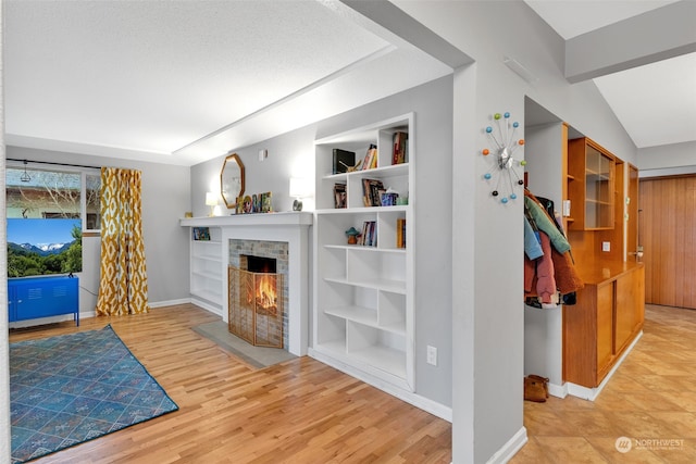 living room featuring built in shelves, light wood-type flooring, and a stone fireplace