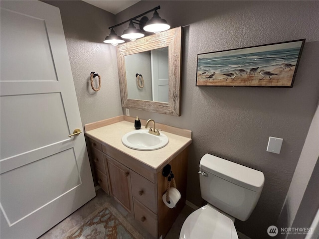 bathroom with a textured wall, vanity, and toilet