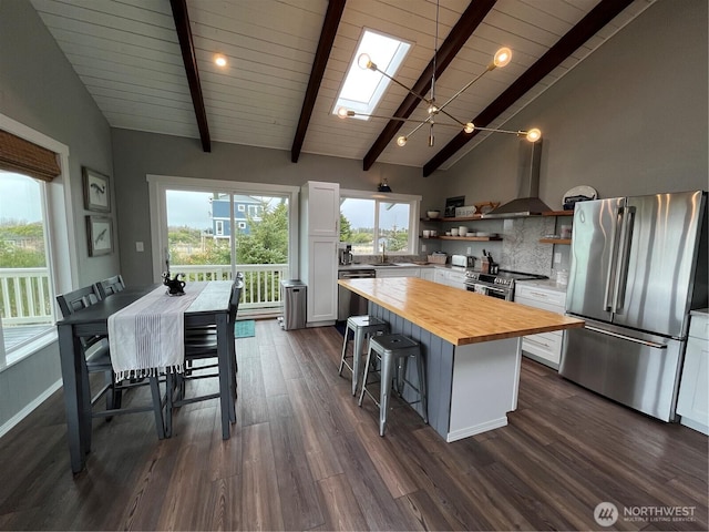 kitchen with stainless steel appliances, butcher block countertops, open shelves, a skylight, and wall chimney exhaust hood