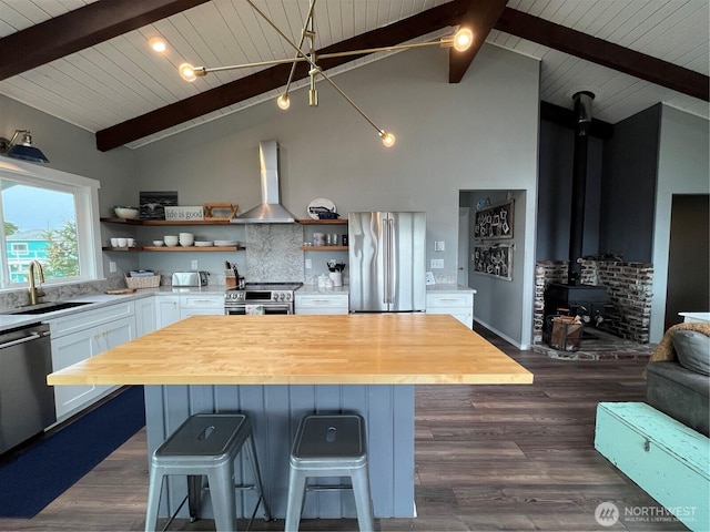 kitchen featuring open shelves, stainless steel appliances, a wood stove, a sink, and wall chimney exhaust hood