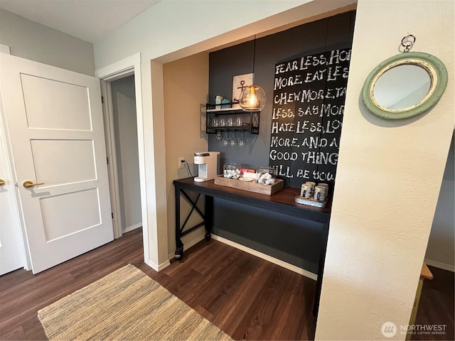 bar with a bar, baseboards, and dark wood-style flooring