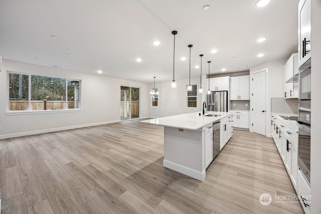 kitchen with white cabinetry, light hardwood / wood-style floors, tasteful backsplash, hanging light fixtures, and a large island with sink