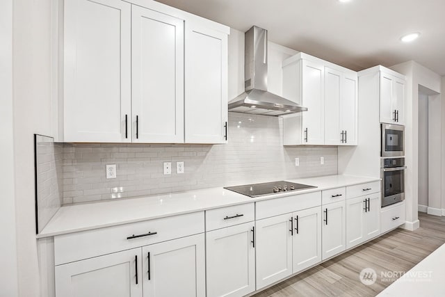 kitchen with white cabinetry, decorative backsplash, black electric cooktop, and wall chimney range hood