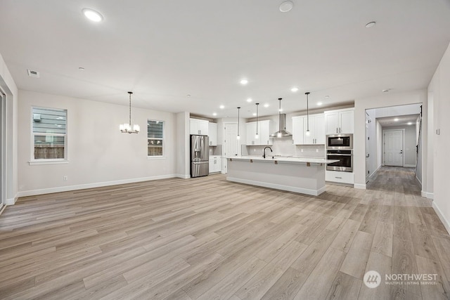 kitchen with decorative light fixtures, white cabinets, appliances with stainless steel finishes, and wall chimney range hood