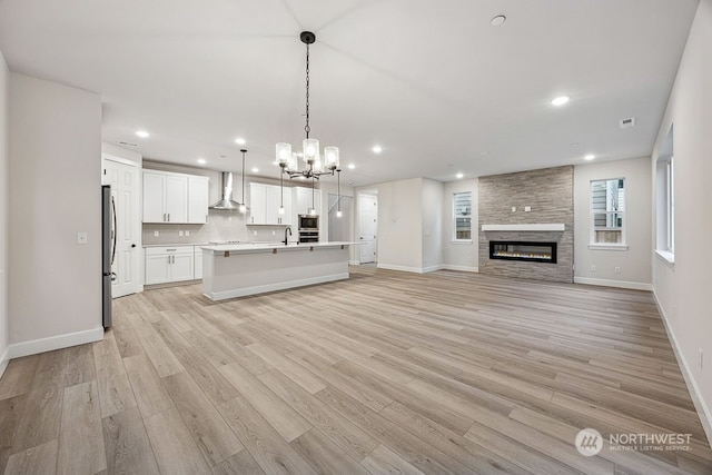 kitchen featuring wall chimney exhaust hood, stainless steel appliances, tasteful backsplash, hanging light fixtures, and a center island with sink