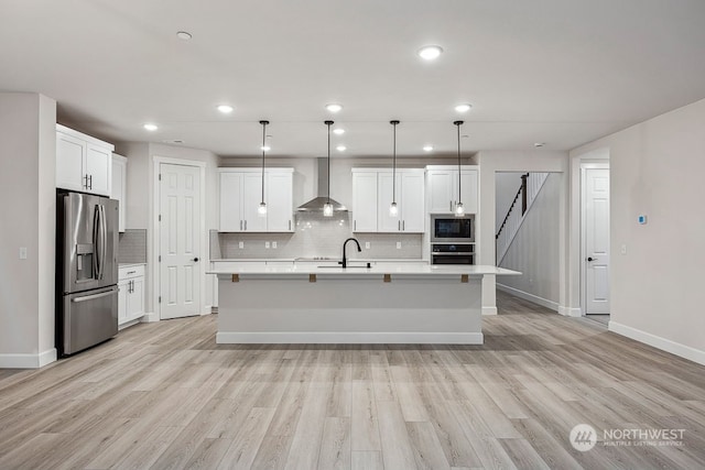 kitchen with stainless steel appliances, wall chimney exhaust hood, a kitchen island with sink, and decorative light fixtures