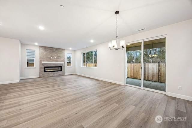 unfurnished living room featuring a large fireplace, a notable chandelier, and light hardwood / wood-style flooring