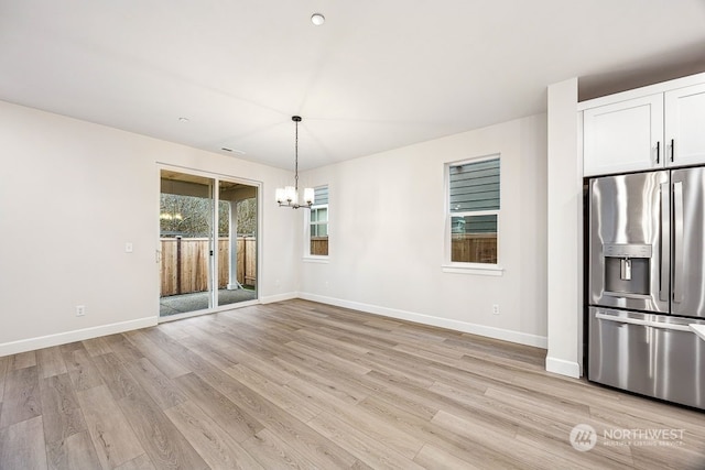 unfurnished dining area featuring an inviting chandelier and light hardwood / wood-style flooring