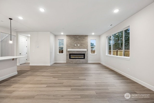 unfurnished living room with light hardwood / wood-style floors and a stone fireplace