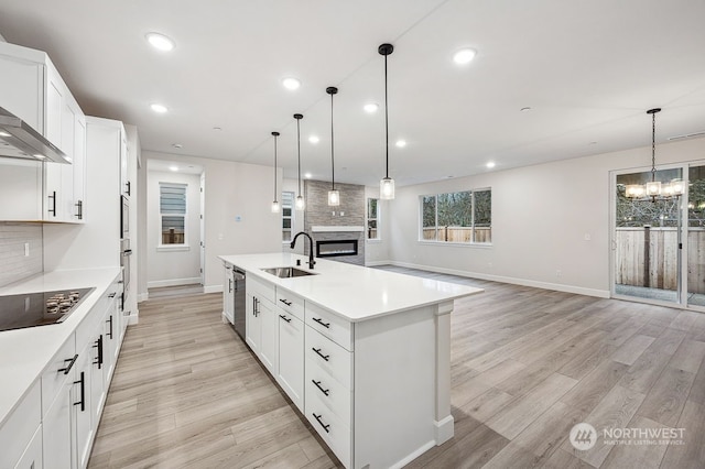 kitchen featuring black electric stovetop, a kitchen island with sink, hanging light fixtures, and sink