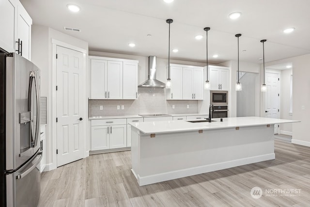 kitchen with decorative light fixtures, wall chimney range hood, sink, stainless steel appliances, and white cabinets